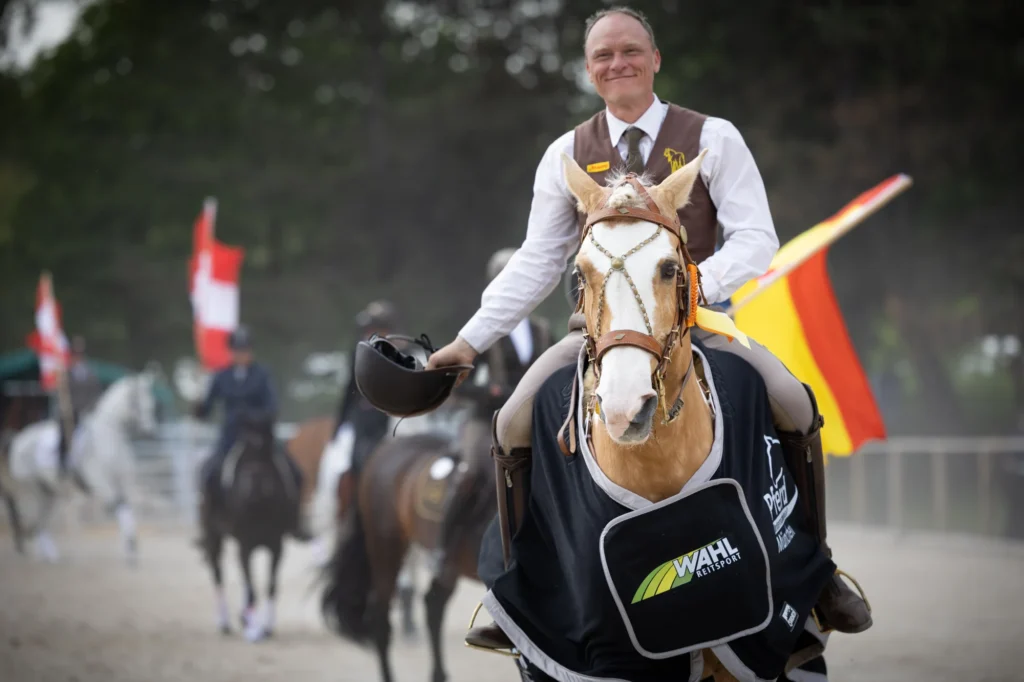 Reiter auf einem beige weiß gescheckten Pferd reitet frontal auf die kamera zu